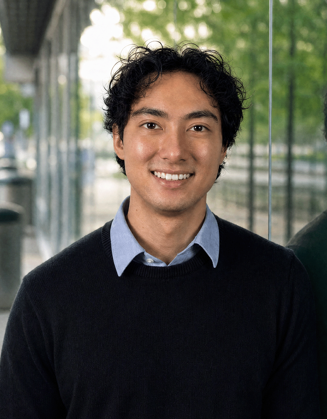 Benjamin Hadler smiling in front of a glass wall with trees in the background